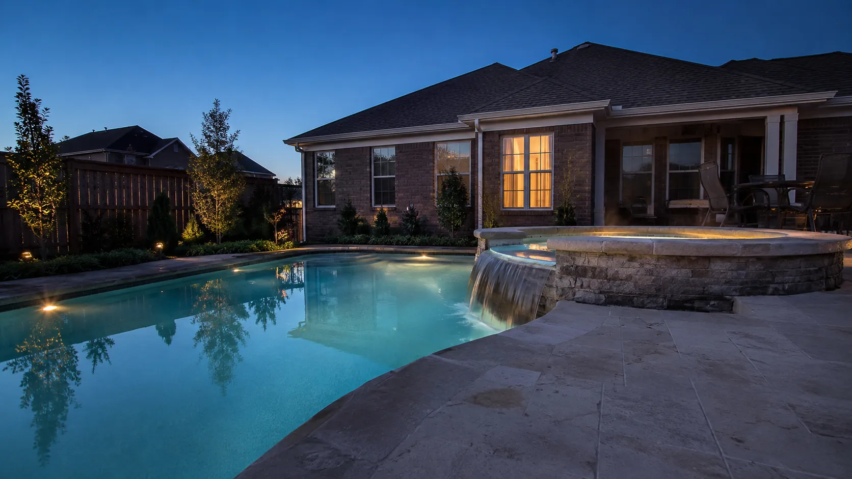 Newly finished gunite pool with a raised spa and stone coping in a residential back yard at dusk